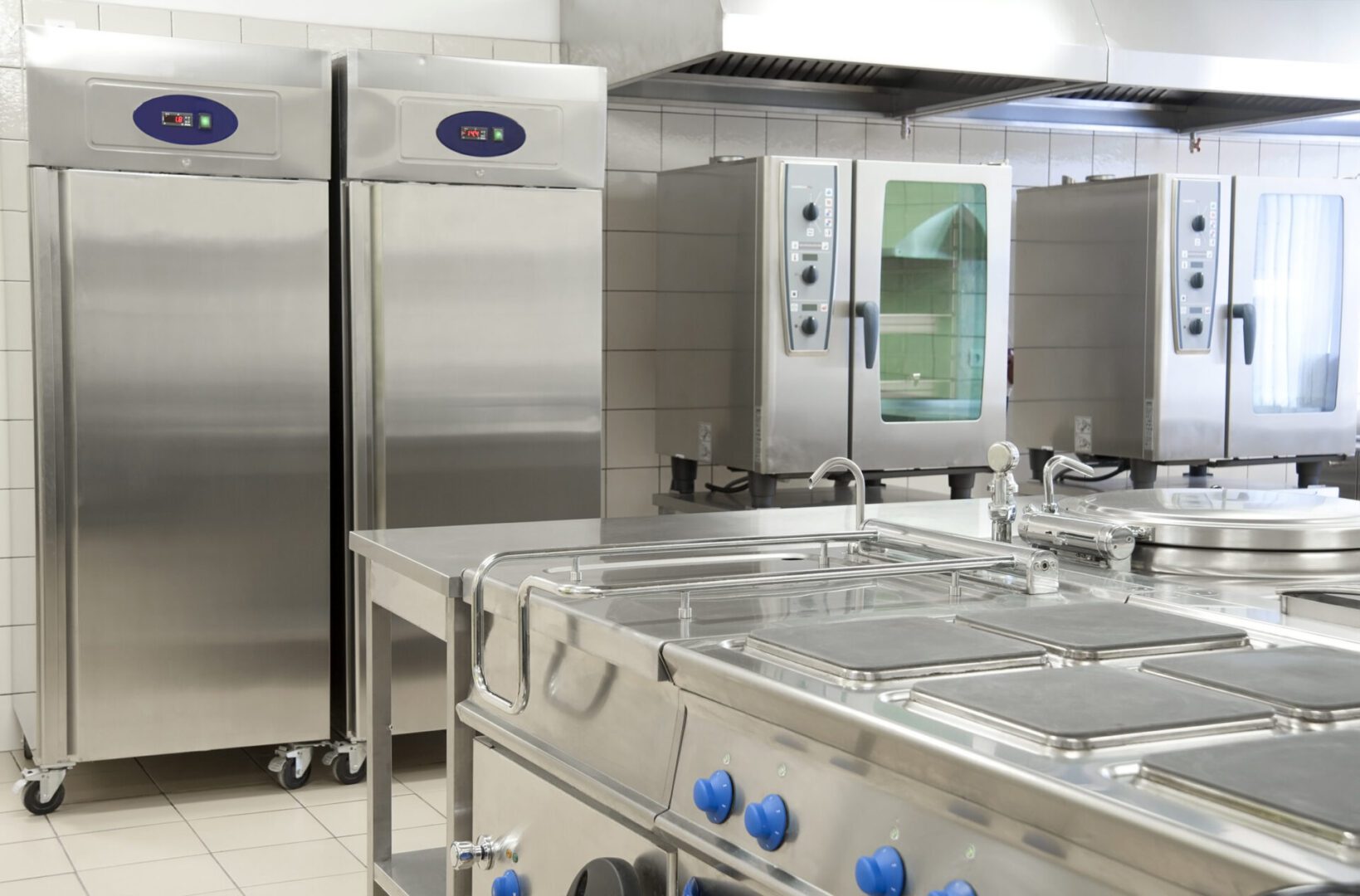 Empty restaurant kitchen with professional equipment A kitchen with stainless steel appliances and blue knobs.